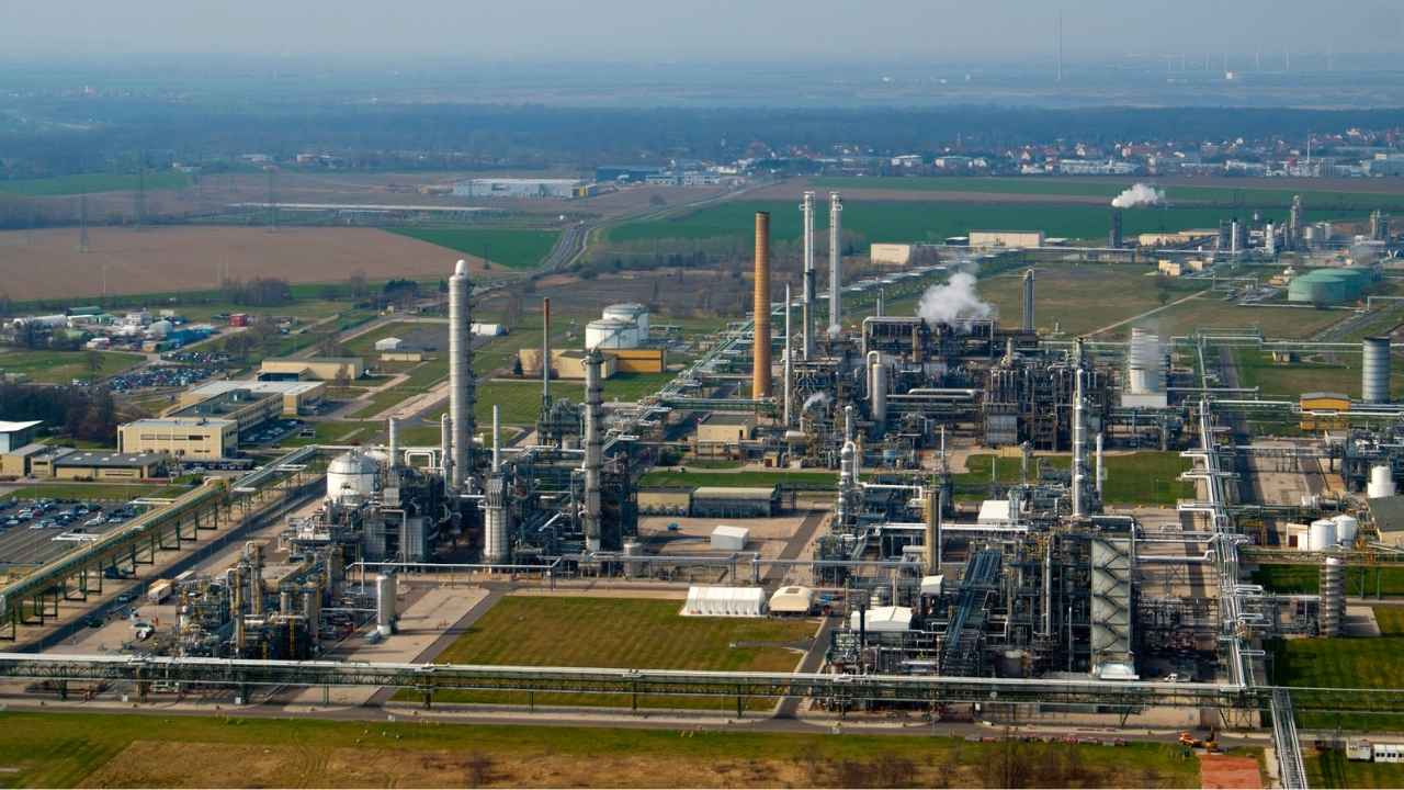 Aerial view of a sprawling industrial petrochemical refinery facility showing processing units, pipelines, storage tanks, and perimeter security boundary infrastructure.